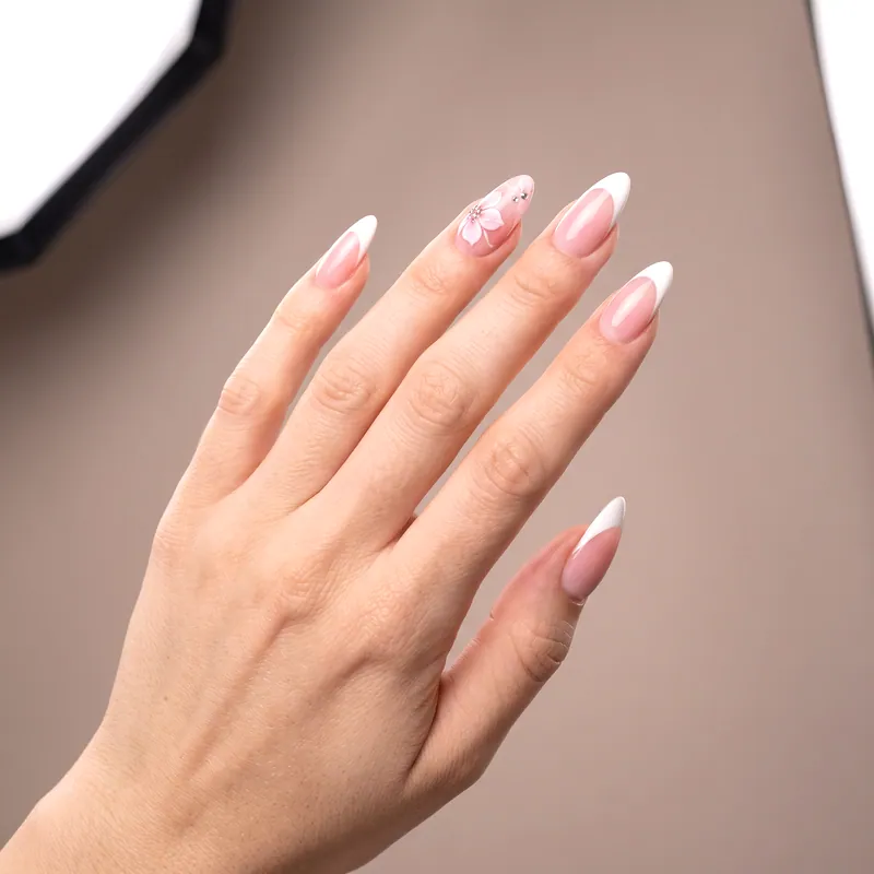 Uñas almendradas largas con French blanco sobre base rosa y una flor rosa pintada a mano con cristales en el anular