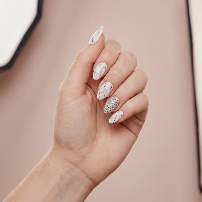 Uñas almendradas medianas con efecto mármol blanco, vetas grises y una uña cubierta de cristales transparentes