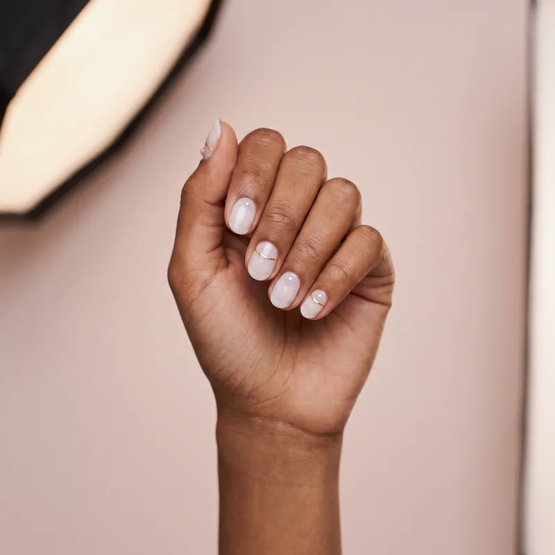 Uñas cortas redondas en blanco lechoso con perlitas aplicadas y líneas doradas finas