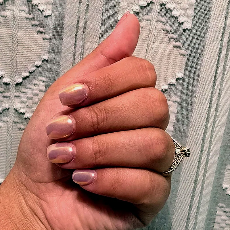 Uñas cortas ovaladas en tono nude con acabado chrome perlado, sobre una cortina de tejido crema